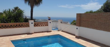 Una piscina amb vista al mar, envoltada per un mur blanc i una tanca de fusta.