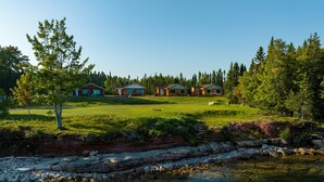 A lakeside property with cabins, clear water, and surrounding greenery. - The Beachcomber at Dockside Resort - Near Bohemia and Trails (Lake Linden)
