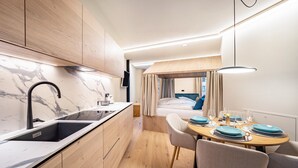 A compact kitchen with a modern design, a dining area with a table set for two, and a visible bed in the background. - Studio Apartment 'Avia Living Elisabeth' with Mountain View and Wi-Fi (Brunico)