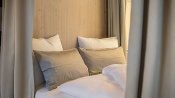 A bed with white bedding and beige pillows, a wooden headboard, and curtains partially drawn.