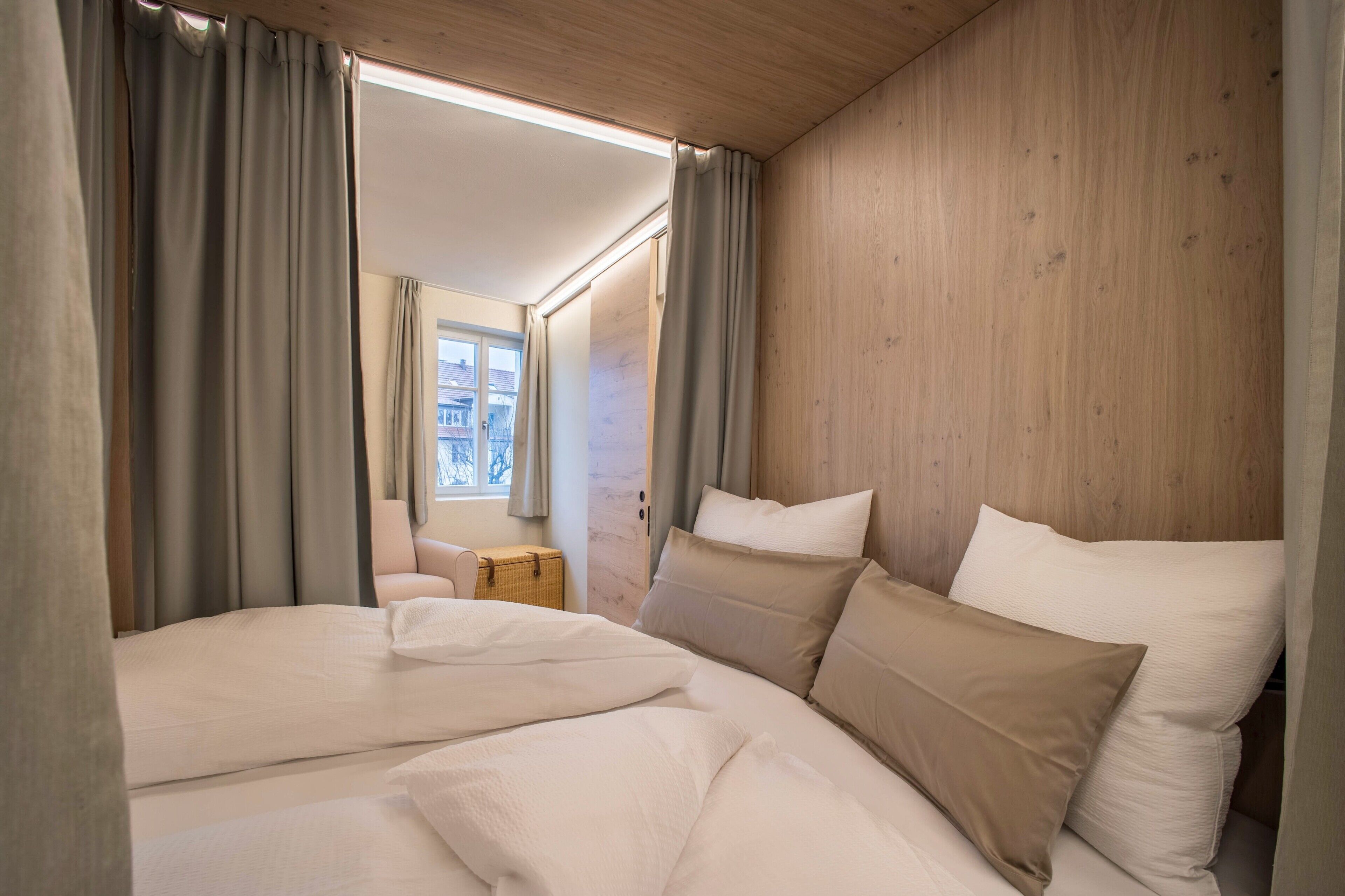 Ein Schlafzimmer mit Bett, Vorhängen, einem Holzkopfende, einem kleinen Tisch und einem Fenster.