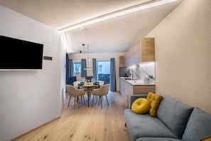 A modern living space with a dining area, a kitchenette, and a flat-screen TV mounted on the wall.