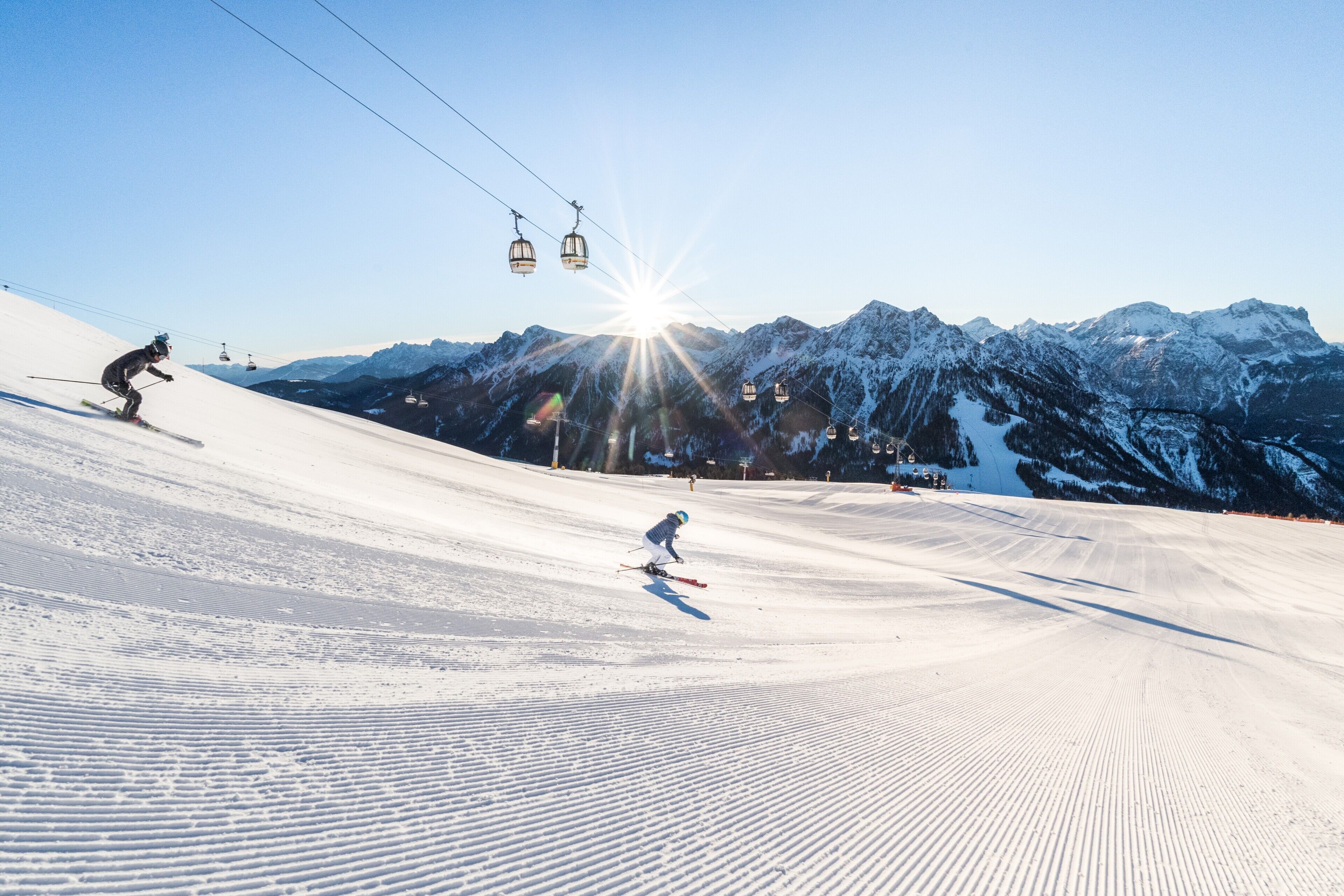 A ski slope with skiers, a ski lift, and snow-covered mountains.