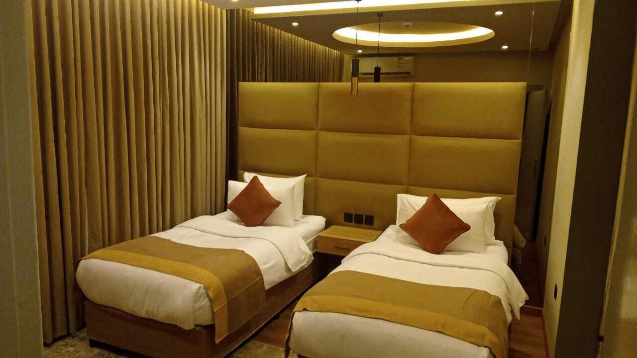 A hotel room with two beds, each with a headboard, a bedside table, and a lamp.