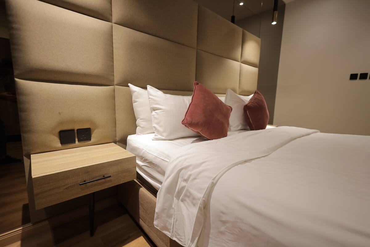A modern bedroom with a tufted headboard, a wooden nightstand, and a bed with white bedding and two pillows.