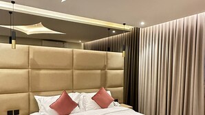 Un dormitorio moderno con cabecera capitonada, una cama grande con ropa de cama blanca y marrón, una mesita de noche y un ventanal con cortinas.