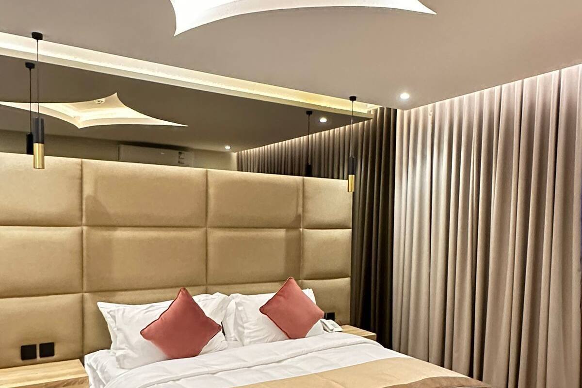 A modern bedroom with a tufted headboard, a large bed with white and brown bedding, a bedside table, and a large window with curtains.