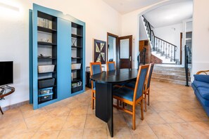 A dining area with a black table and blue chairs, a blue shelving unit, and a staircase leading to a second floor.