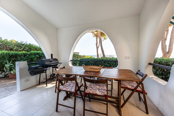 An outdoor patio with a table and chairs, a grill, and a view of the sea.