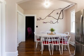 A dining area with a white table and chairs, a chandelier, and a wall-mounted branch decoration. - Bachelorette Paradise -Hot Tub*Near Dwntn*Fire Pit (Asheville)