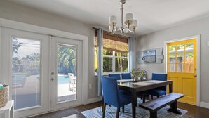 A dining area with a table, chairs, and a bench. There is a window with blinds, a door, and a chandelier. - Lush Tropical Oasis! HEATED Pool, 1 mile to downtown, 2 miles to public beach (Lake Worth Beach)