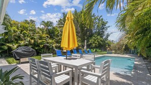A poolside area with a table and chairs, a yellow umbrella, and a barbecue grill. - Lush Tropical Oasis! HEATED Pool, 1 mile to downtown, 2 miles to public beach (Lake Worth Beach)