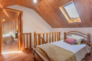 A bedroom with a wooden ceiling, a skylight, a bed with a patterned pillow, and a view of another room.