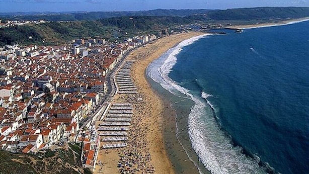 Luftaufnahme einer Küstenstadt mit Strand, Gebäuden und blauem Himmel.