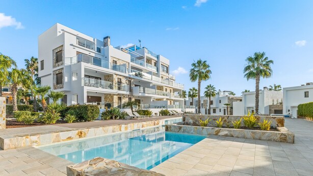 A modern building with a swimming pool, palm trees, and a clear sky. - Apartment 'Casa Marysol' with Sea View, Wi-Fi and Air Conditioning (Orihuela)
