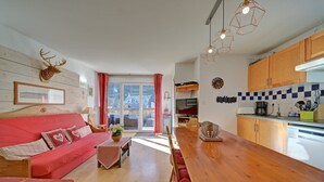 Ein zeitgemäßer Wohnraum mit Esstisch aus Holz, rotem Sofa und Küchenbereich mit Holzausziehtischen und einer gefliesten Spritzwand.