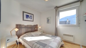 Ein Schlafzimmer mit Bett, Schreibtisch mit Lampe, Fenster mit Blick und Heizkörper.