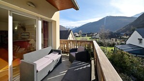 Ein Balkon mit Korbmöbeln, einer Schiebetür und Blick auf eine Berglandschaft.