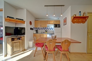 A compact kitchen with wooden cabinets, a dining table with chairs, a television, and a microwave.