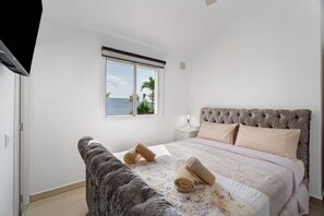 Un dormitorio con cama, mesita de noche, ventana y vista al mar.