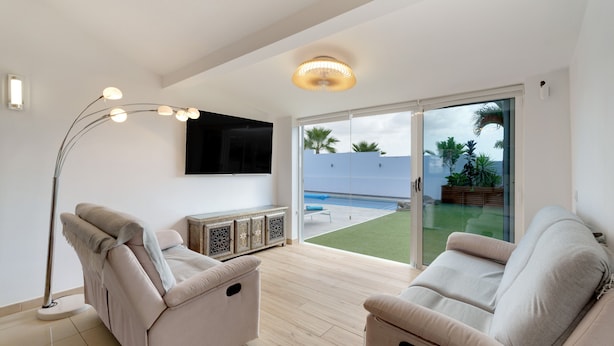Un salon moderne avec deux canapés, une lampe sur pied, un téléviseur à écran plat et une porte-fenêtre coulissante donnant sur une piscine.