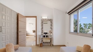 Une chambre d’hôtel avec deux lits, une coiffeuse avec un miroir, une fenêtre donnant sur un paysage agréable et une porte menant à une autre chambre.