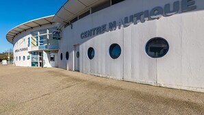 Ein Gebäude mit einem Schild, auf dem 'CENTRE NAUTIQUE' steht, mit einer gewölbten Fassade, runden Fenstern und einem überdachten Eingang.