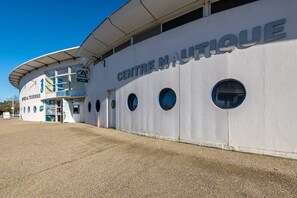 Un bâtiment sur lequel on peut lire l’inscription « CENTRE NAUTIQUE », caractérisé par une façade incurvée dotée de fenêtres rondes et une entrée abritée.