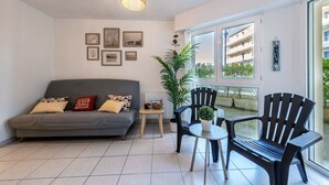 Ein Wohnzimmer mit grauem Sofa, zwei schwarzen Sesseln, einem kleinen Tisch mit Pflanze und einem großen Fenster.