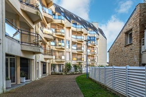 Un immeuble résidentiel à plusieurs étages, doté de balcons, d’une allée en gravier et d’une clôture blanche.