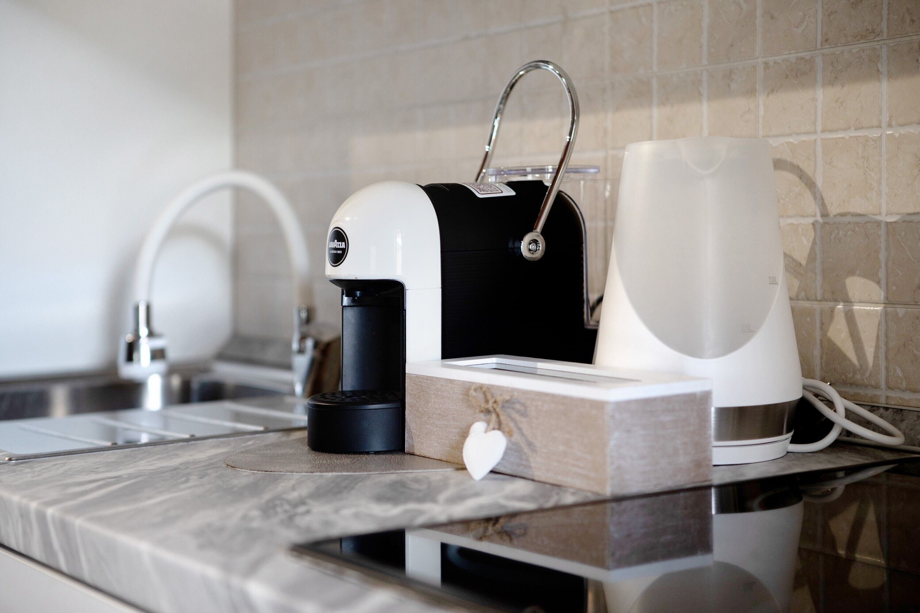 A kitchen with a coffee maker, a kettle, and a water dispenser on a marble countertop.