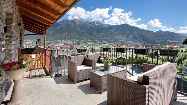 Ein Balkon mit Korbmöbeln, einer Steinmauer und Blick auf Berge.