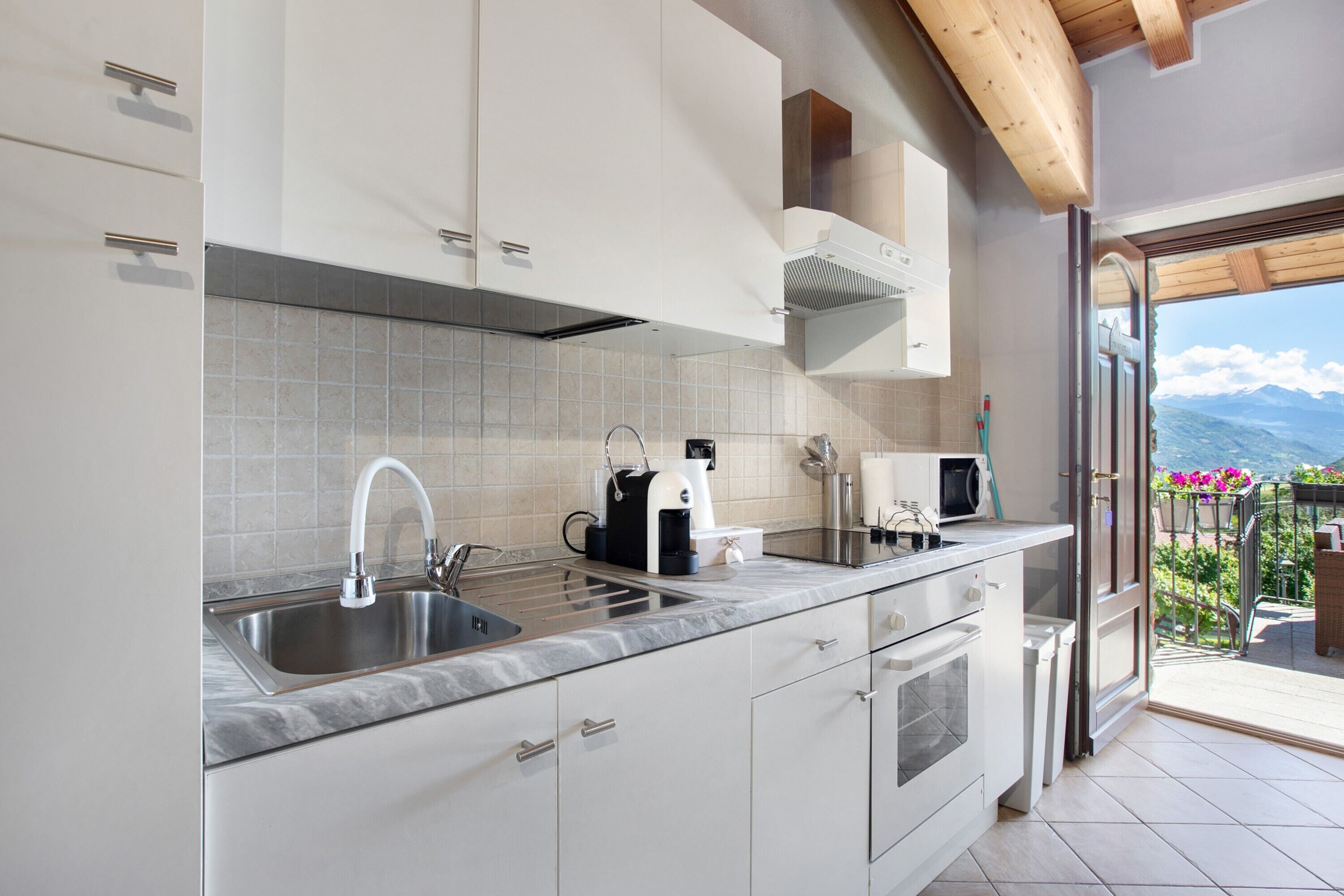 A kitchen with a sink, stove, and coffee maker, leading to a balcony with a view.
