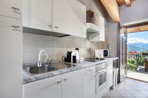 A kitchen with a sink, stove, and coffee maker, leading to a balcony with a view.