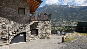 Ein Steinhaus mit einem hölzernen Balkon, einem steinernen Bogen und Blick auf Berge.