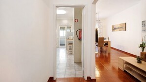Ein Flur mit einer Holzbank, einem kleinen Tisch und einem Stuhl. Eine Tür führt in einen anderen Raum mit einem Fenster und einem an der Wand befestigten Feuerlöscher.