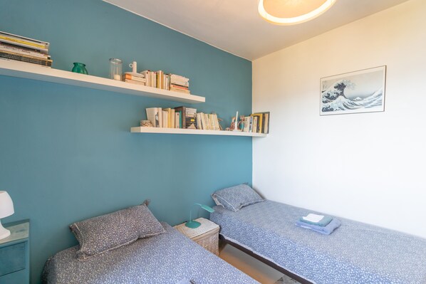 A bedroom with two beds, a bookshelf, a wall-mounted picture, and a bedside table with a lamp. - Villa "Mon Nid d'Aigle" with Private Terrace & Wi-Fi (Olmeto)