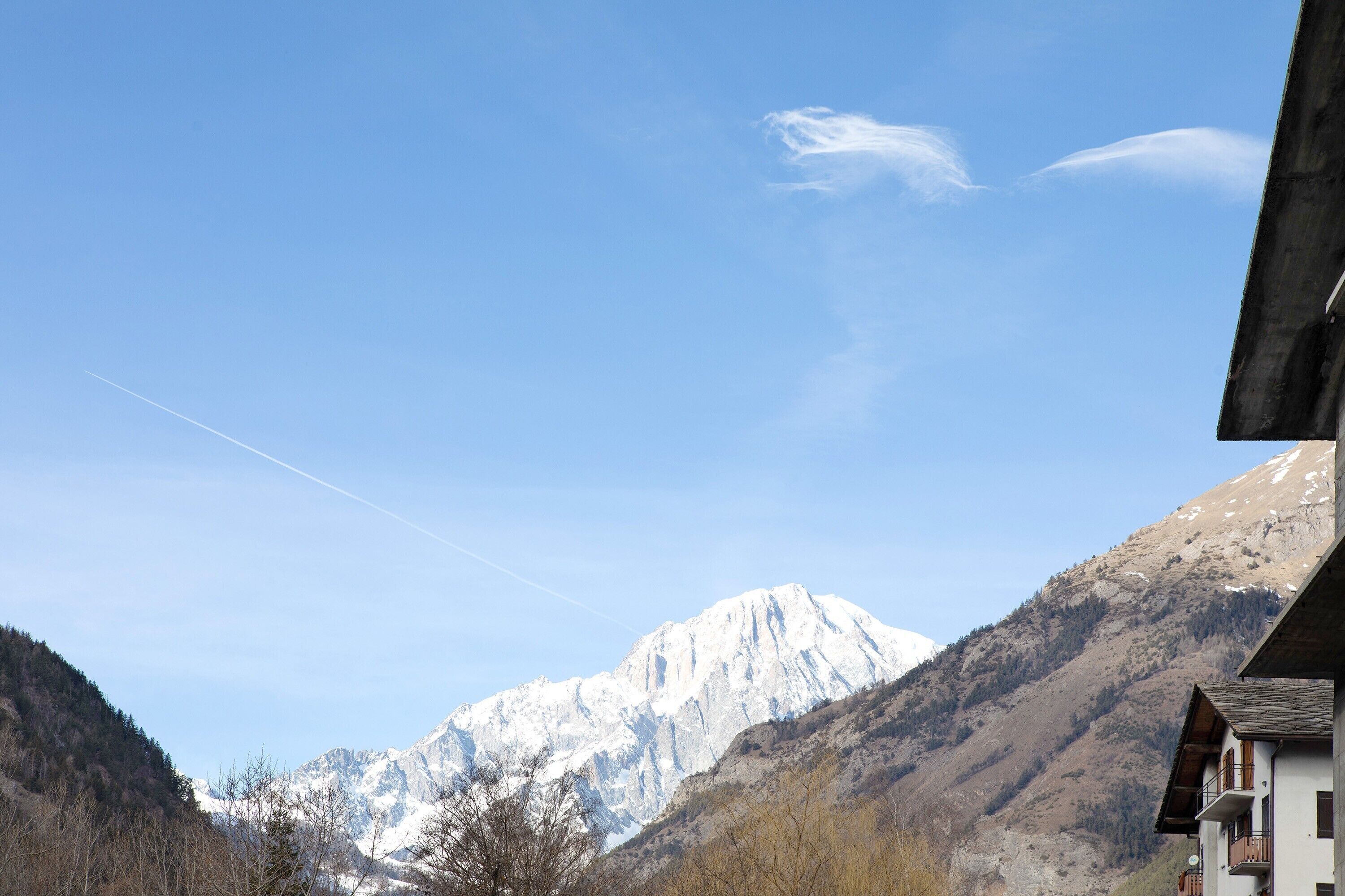 A mountain with a snow-capped peak, a clear sky, and a building with a balcony.