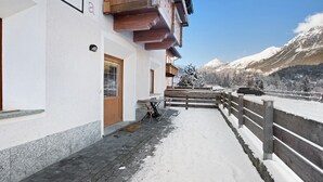 A snow-covered outdoor area with a wooden fence, a building with a wooden balcony, and a mountain view. - Holiday Apartment "Tra-Monti E Mare" with Mountain View, Private Terrace & Sauna (Valdidentro)