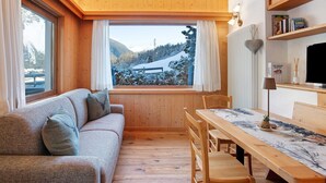 A cozy room with a wooden floor, a sofa, a dining table, and a window with a view of a snowy landscape. - Holiday Apartment "Tra-Monti E Mare" with Mountain View, Private Terrace & Sauna (Valdidentro)