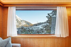 Un interno in legno con un'ampia finestra che si affaccia su un paesaggio montano innevato.