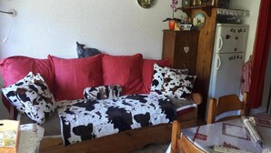 A room with a wooden sofa, a red and black cow print blanket, a wooden cabinet, and a table with a patterned tablecloth.
