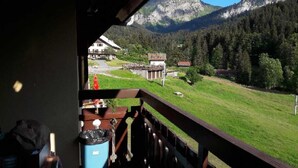 A balcony with a view of a mountain landscape, a building with a red roof, and a grassy area.