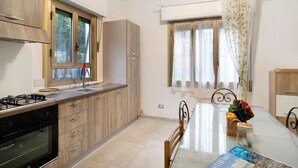 Une cuisine moderne avec des meubles en bois, une cuisinière à gaz et un coin repas comprenant une table et des chaises en verre.