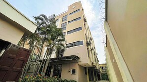 Un edificio de varios pisos con fachada plana, varias ventanas y un pequeño acceso con puerta y plantas en macetas.