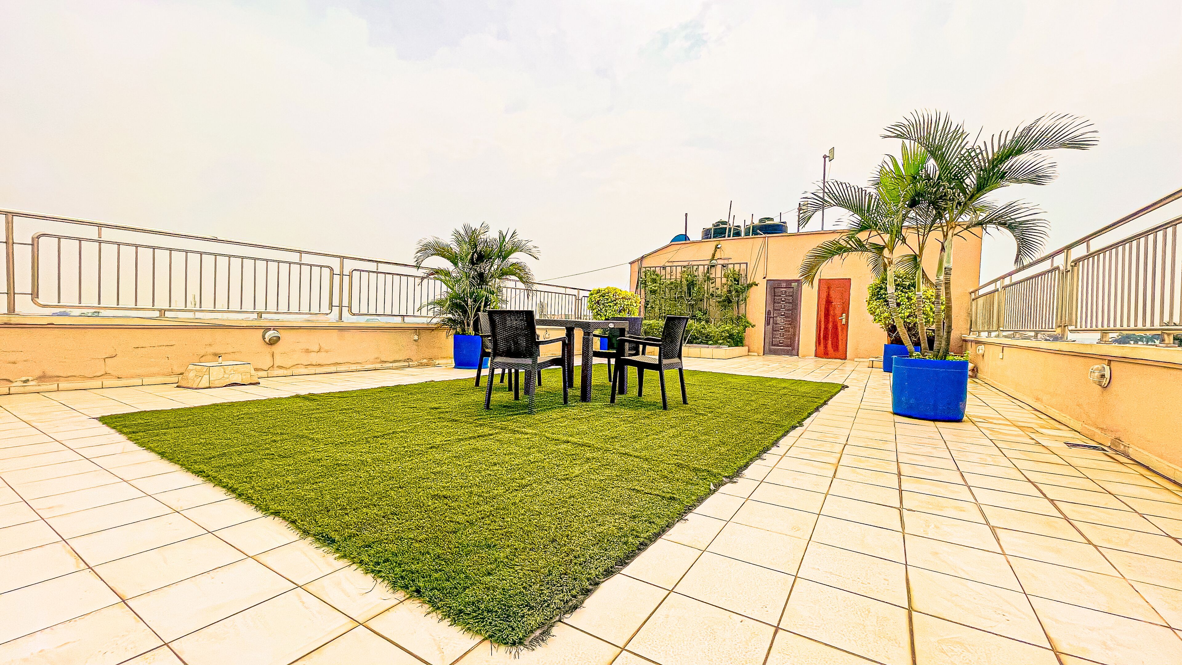 Terraço no telhado com gramado, mesa e cadeiras, e plantas em vasos.
