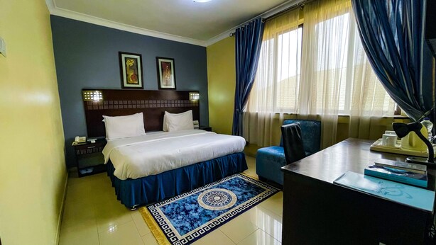 Habitación de hotel con cama, escritorio, silla, mesita de noche y dos lámparas de pared.