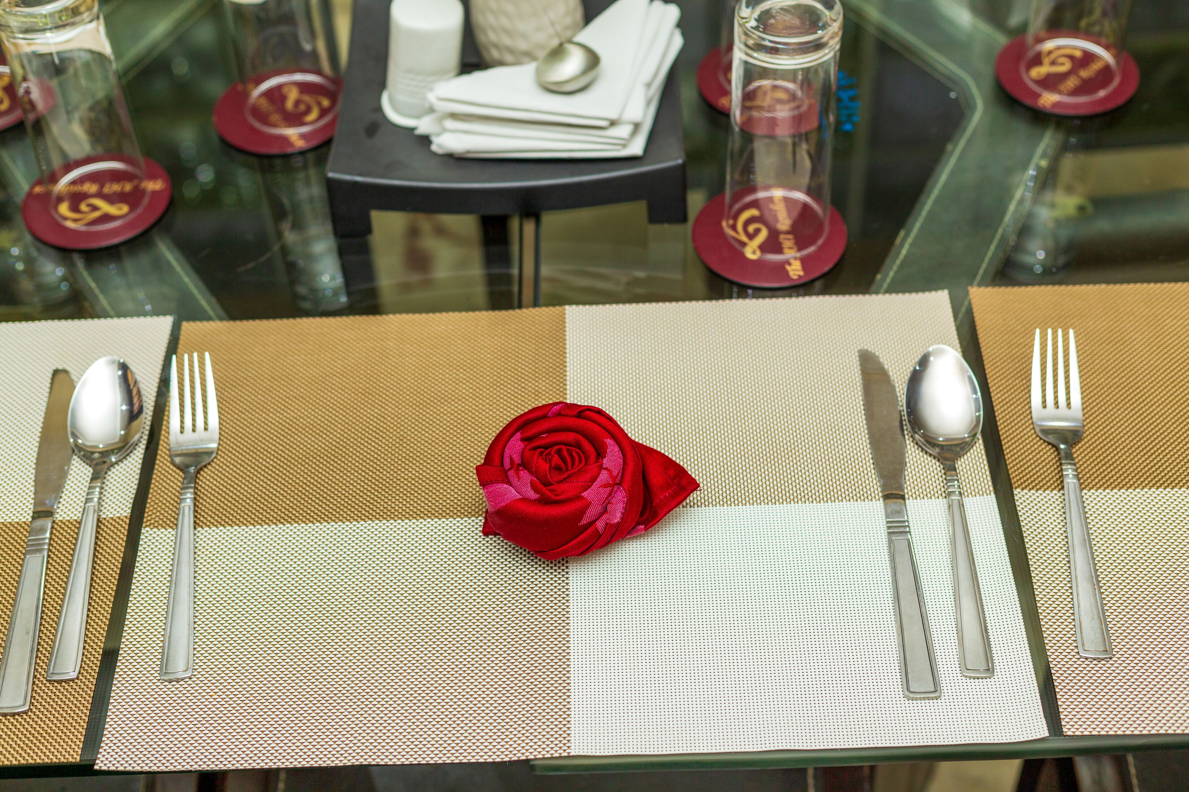 Une table dressée avec un bouquet de roses rouges en guise de centre de table, des couverts en argent et de la verrerie, le tout posé sur un set de table texturé.