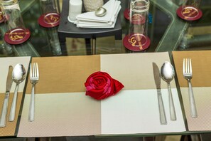 A table set with a red rose centerpiece, silverware, and glassware on a textured placemat.