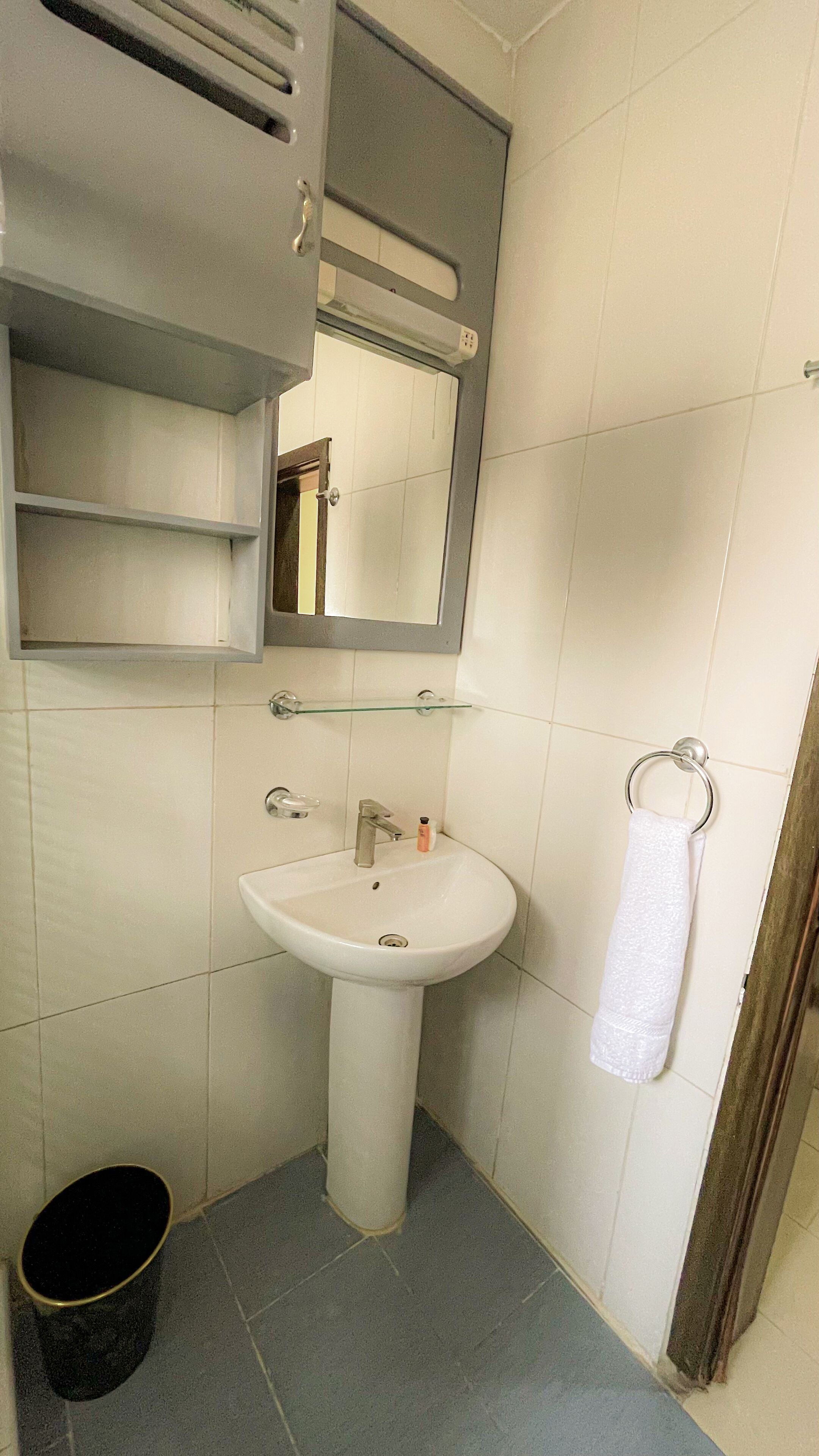 Een badkamer met een wastafel op een zuil, een spiegel, een handdoekhouder en een prullenbak.